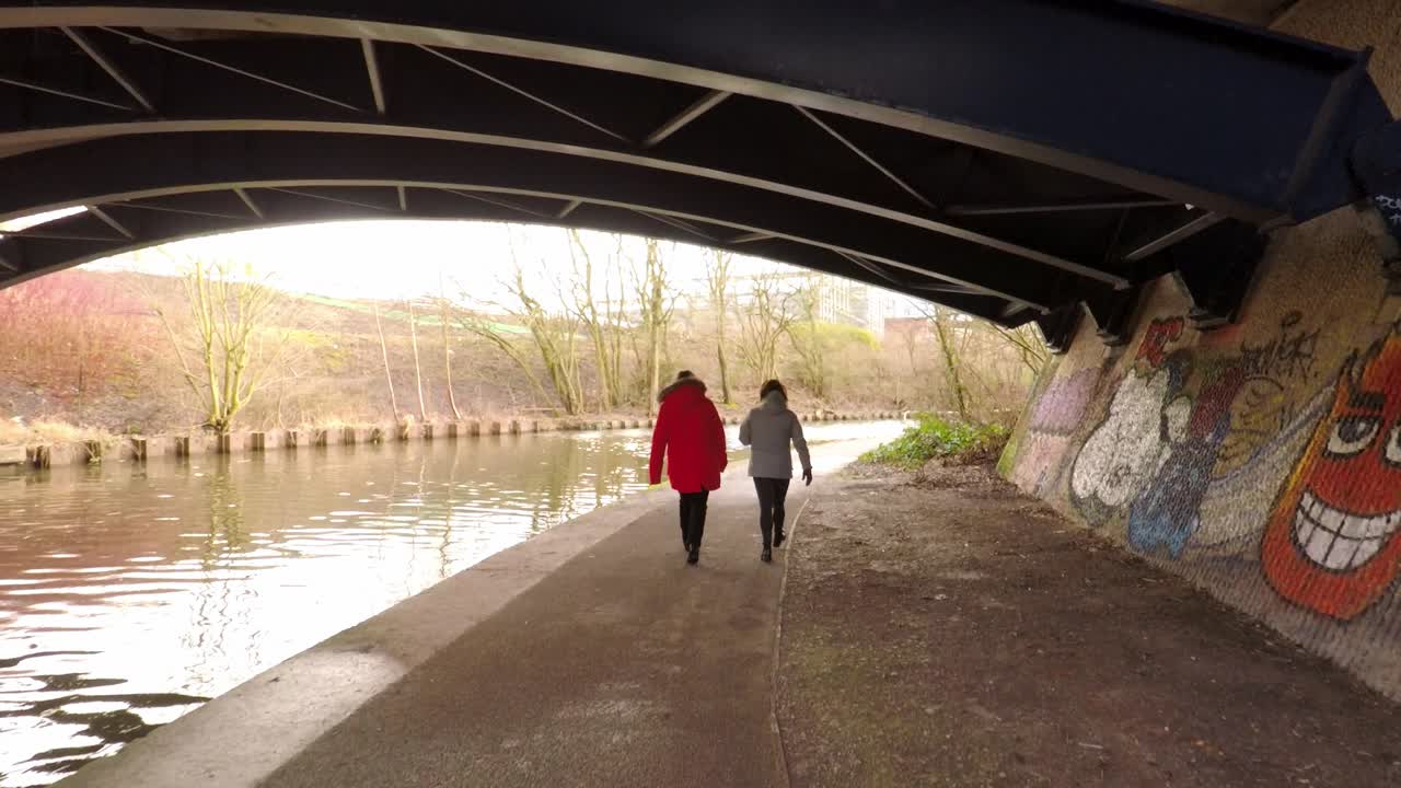 2명의 여성이 운하를 따라 폐허가 된 많은 공장이 있는 빈곤 지역인 스토크 온 트렌트에 있는 이전 산업 운하를 따라 산책합니다.