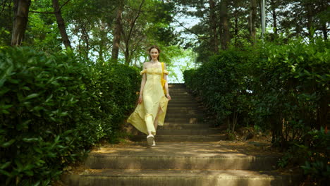 elegant young woman in yellow sundress coming down the stairs in summer park in slow motion