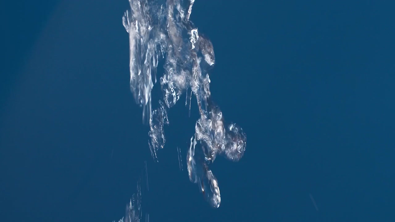 Real pure water flowing down with splashing on blue background shooting in slow motion