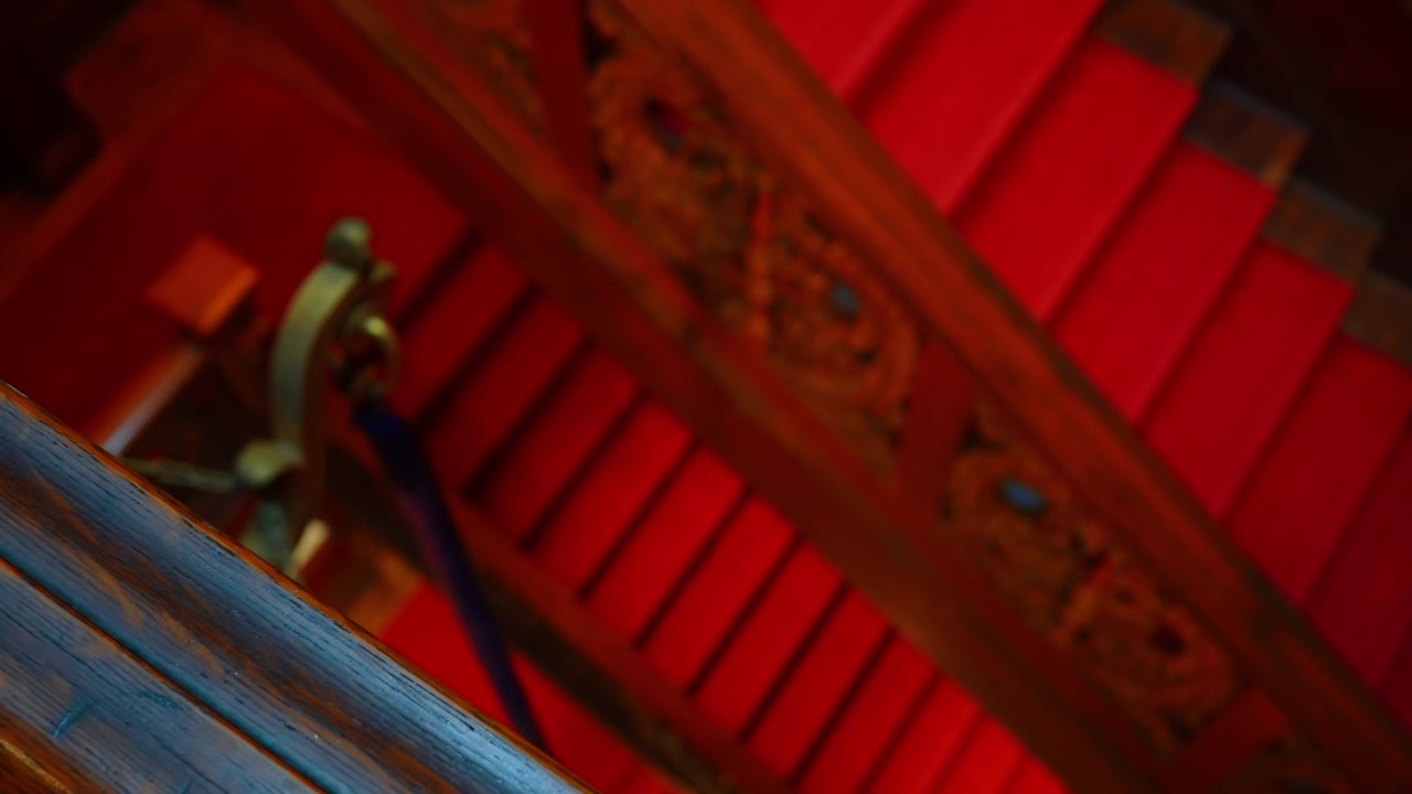 Dettaglio di una scala in legno decorata con tappeto rosso. Primo piano dall'alto di una ringhiera decorativa in legno e scale coperte da una vivace moquette rossa in un edificio classico.