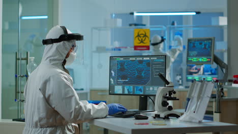 medical scientist in ppe suit working with dna scan image typing on pc