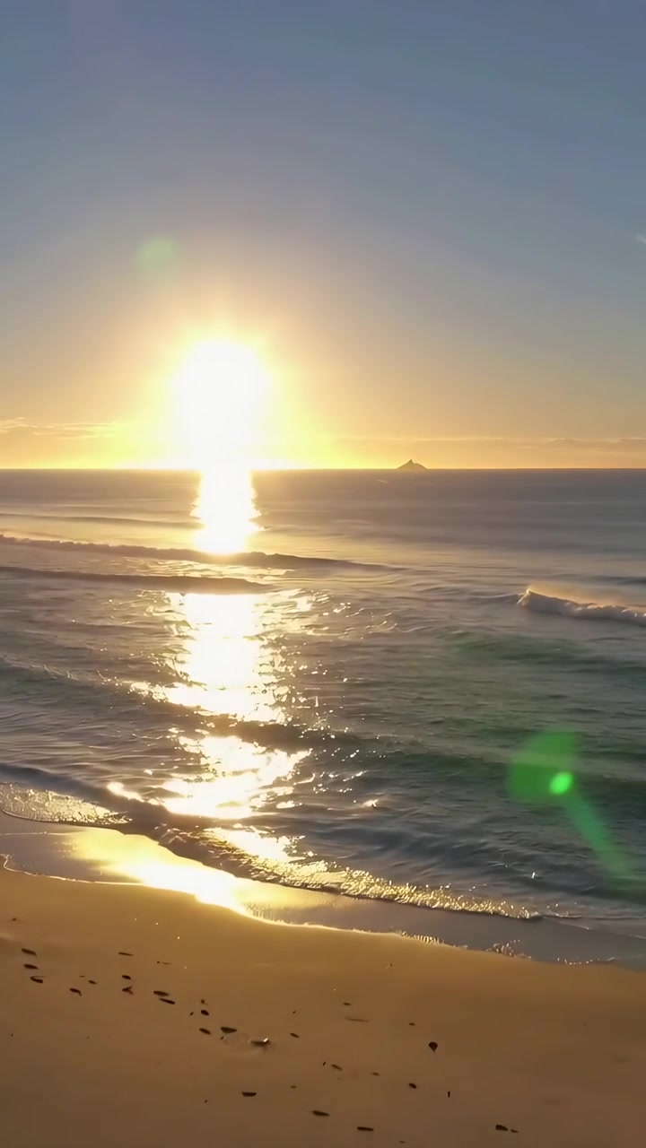 Vídeo vertical: Sol nascendo projetando reflexo vertical na costa com ondas quebrando e pegadas