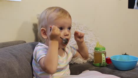 niña lamiendo cuchara en el sofá