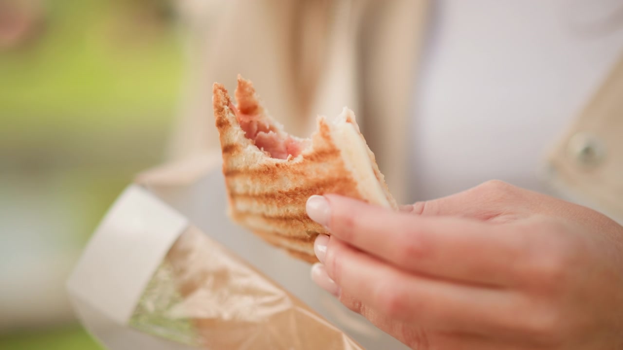 Close up of woman holding and eating open faced sandwich with visible meat filling. subject hand gently manipulates food revealing texture details like toasted bread grill marks