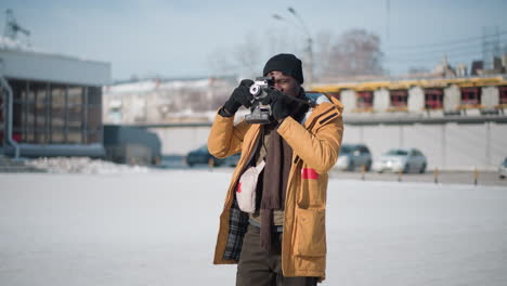 zoom in on snapper fix eyes on viewfinder carefully adjusting lens then reviewing shot on lcd display against snowy urban street lined with parked cars and frosted trees under bright winter sun