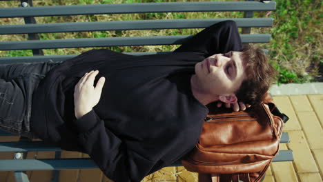 tired man sleeping on his backpack while on a bench outdoor