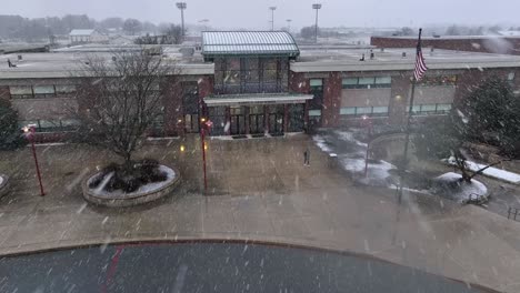 Aerial-approach-towards-student-walking-out-of-American-school-building-during-snow-storm