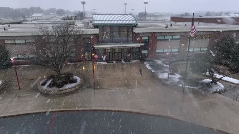 Enfoque-Aéreo-Hacia-El-Estudiante-Que-Sale-Del-Edificio-De-La-Escuela-Americana-Durante-La-Tormenta-De-Nieve