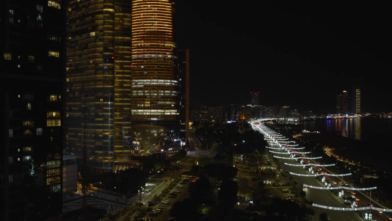 Um drone revela a escala urbana mágica de Abu Dhabi à noite. Deslizando bem ao lado de uma torre escura, ele revela as luzes infinitas da autoestrada costeira e o horizonte moderno da cidade.
