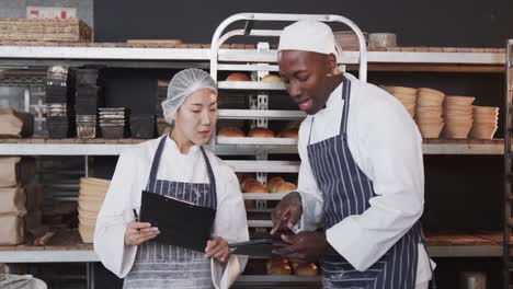 diverse bakers working in bakery kitchen, counting rolls with tablet in slow motion