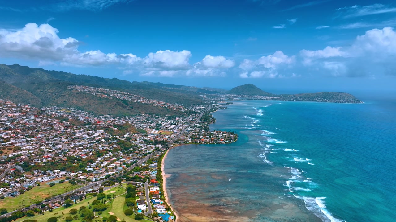 Costa dell'Oceano Pacifico vista dall'alto. Area densamente popolata vicino alla spiaggia. Montagne sullo sfondo. Nuvole bianche nel cielo azzurro. Hawaii, USA