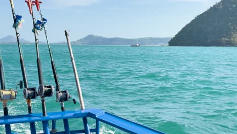 fishing rods on a boat in turquoise waters of chalong bay, phuket. calm sea, clear skies, and distant islands create a serene atmosphere