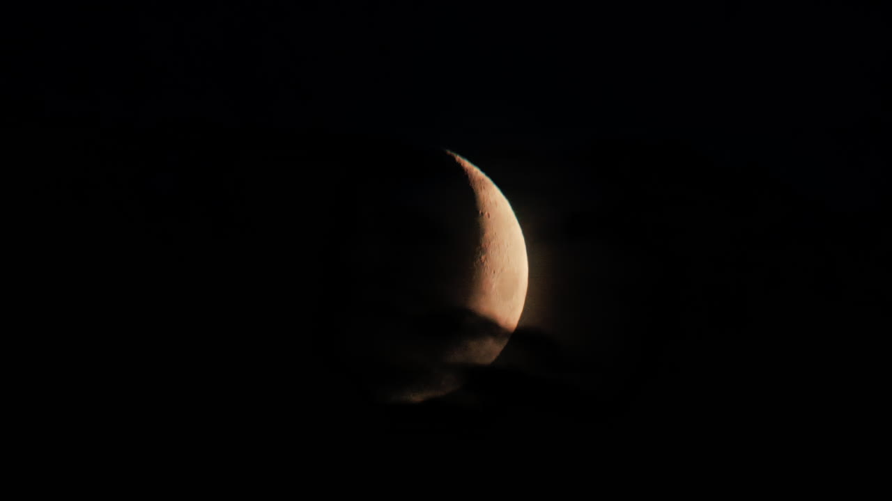 Illuminated crescent moon partially covered by clouds at night