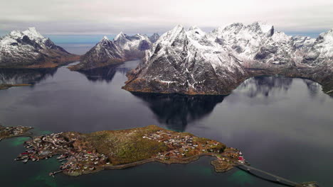aerial view orbiting glacial moskenes mountains and reine fishing village reflecting in winter ocean at sunrise