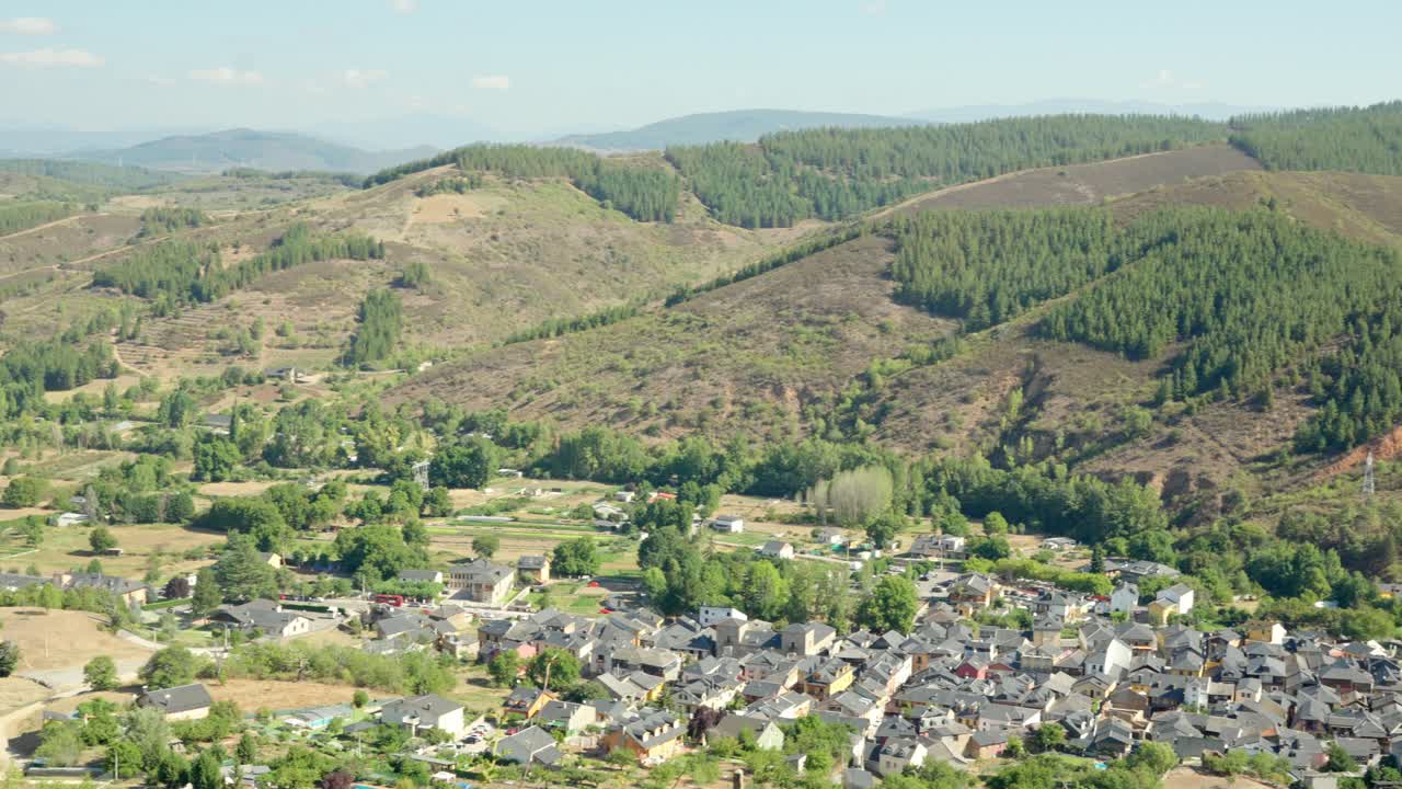 Panoramic view of a village nestled in a green valley surrounded by forested hills