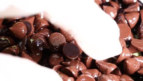 close-up of gloved hands meticulously sorting shiny chocolate chips, highlighting texture and detail.