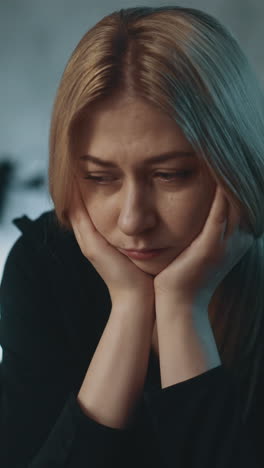 pensive upset blonde lady suffers from tiredness and overworking sitting near table in darkened company office in evening extreme close view slow motion