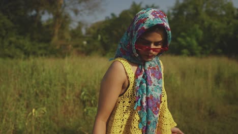 an attractive fashionable asian female wearing a headscarf standing in a field surrounded by lush green grass