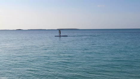 un joven caucásico usa una tabla de remo en el océano en las bahamas.
