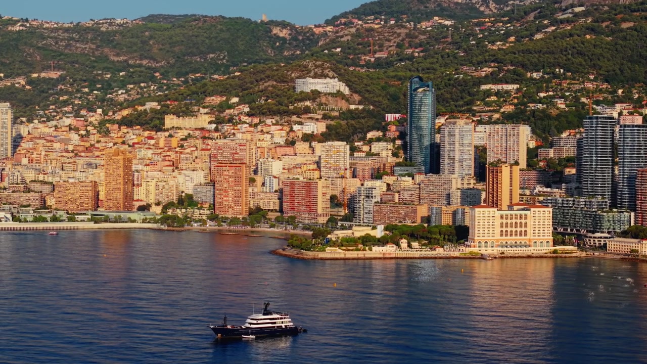 Yacht di lusso che naviga vicino al lungomare di Montecarlo con lo skyline della città e le colline
