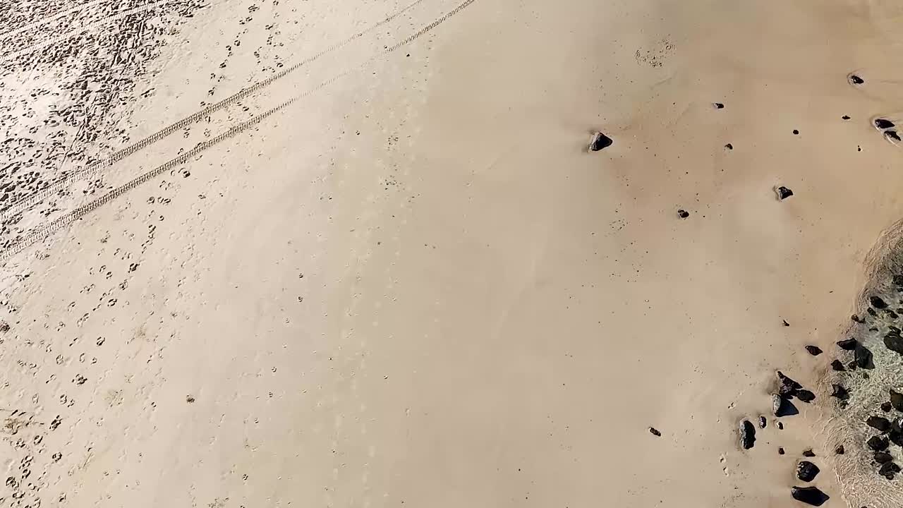 Drone captures intricate patterns of sand and rocks on a serene beach landscape.