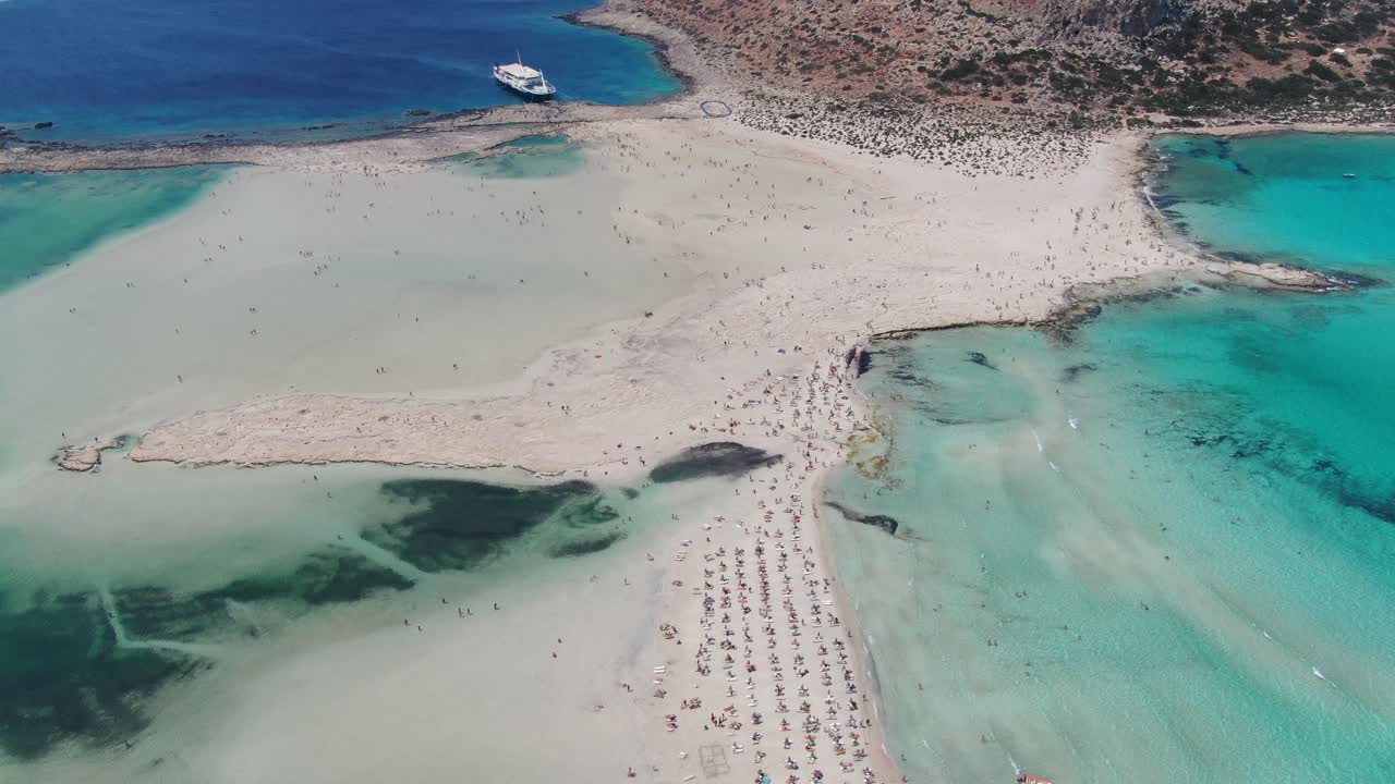 vista de avión no tripulado en grecia volando sobre la playa de balos con mar azul claro a los lados y arena blanca rodeada de paisaje marrón en un día soleado en creta