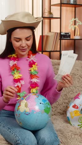 happy woman on sofa with swim ring holding globe and plane tickets planning exciting future trip