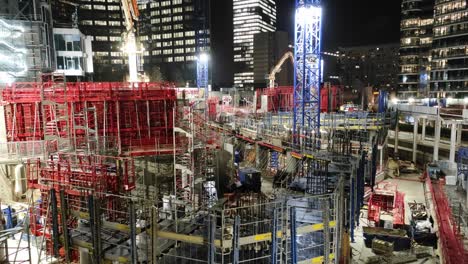 night sight of skyscraper construction site with cranes and scaffolding, wide panning shot