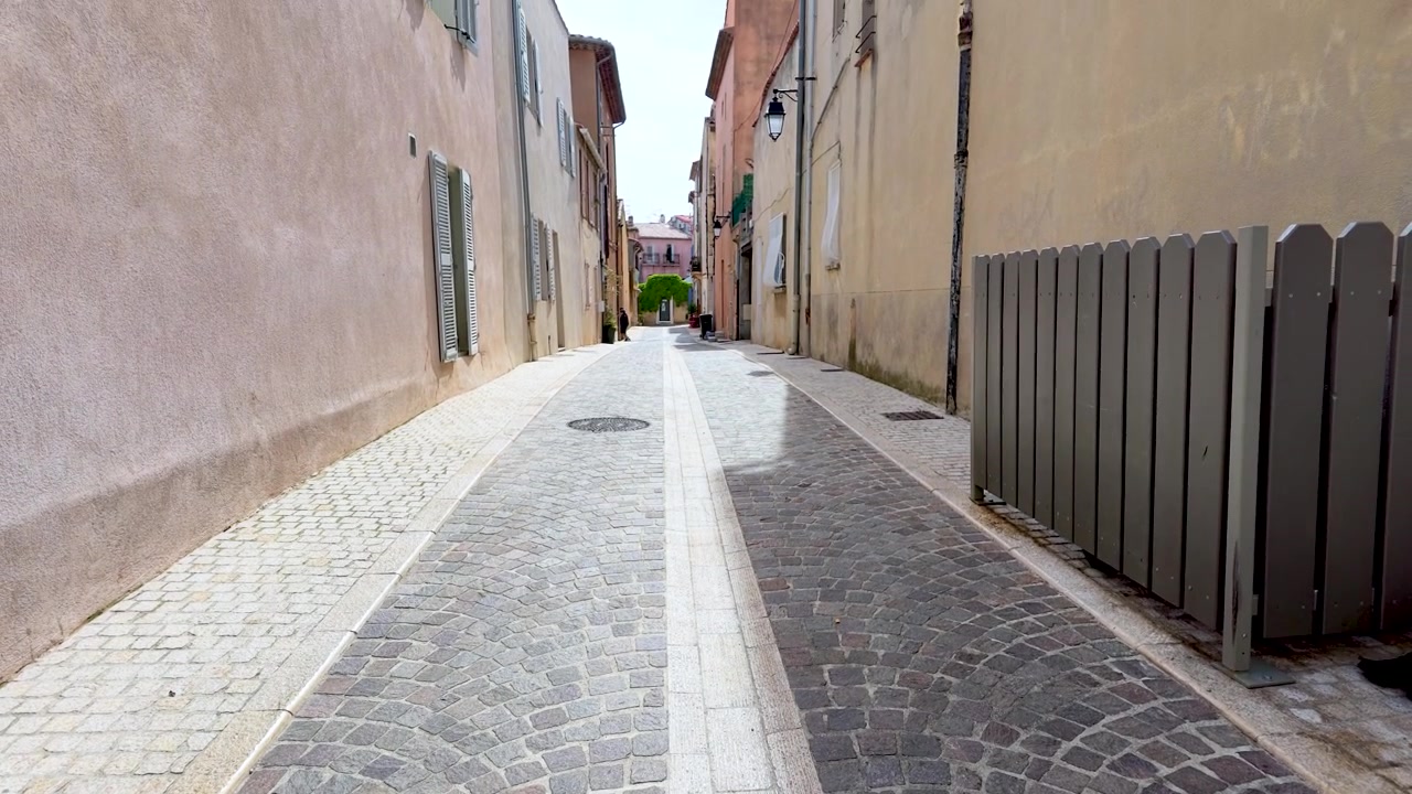 Toma en contrapicado y travelling a través de un tranquilo callejón mediterráneo con persianas y adoquines de piedra