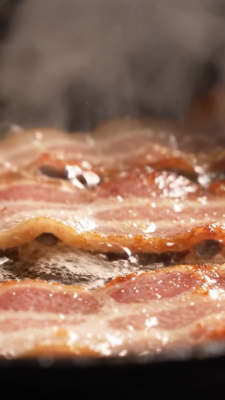 Sprød bacon steger på panden: Et nærbillede af sprøde strimler, der steger til perfektion, og som viser saftigheden og den gyldenbrune farve af hver skive