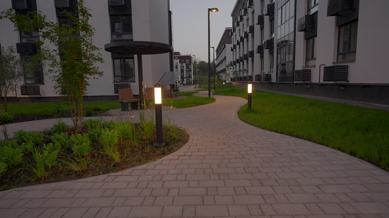 Dusk Courtyard Pathway With Illuminated Bollards Leading Through Landscaped Grounds Between Modern Apartments