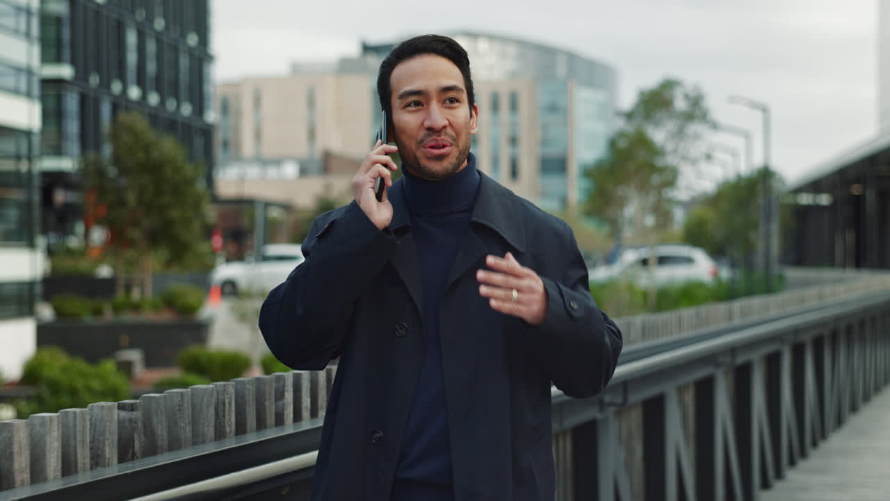 한 남자가 드폰으로 얘기하고 미소 짓고 도시 거리를 고 있다.