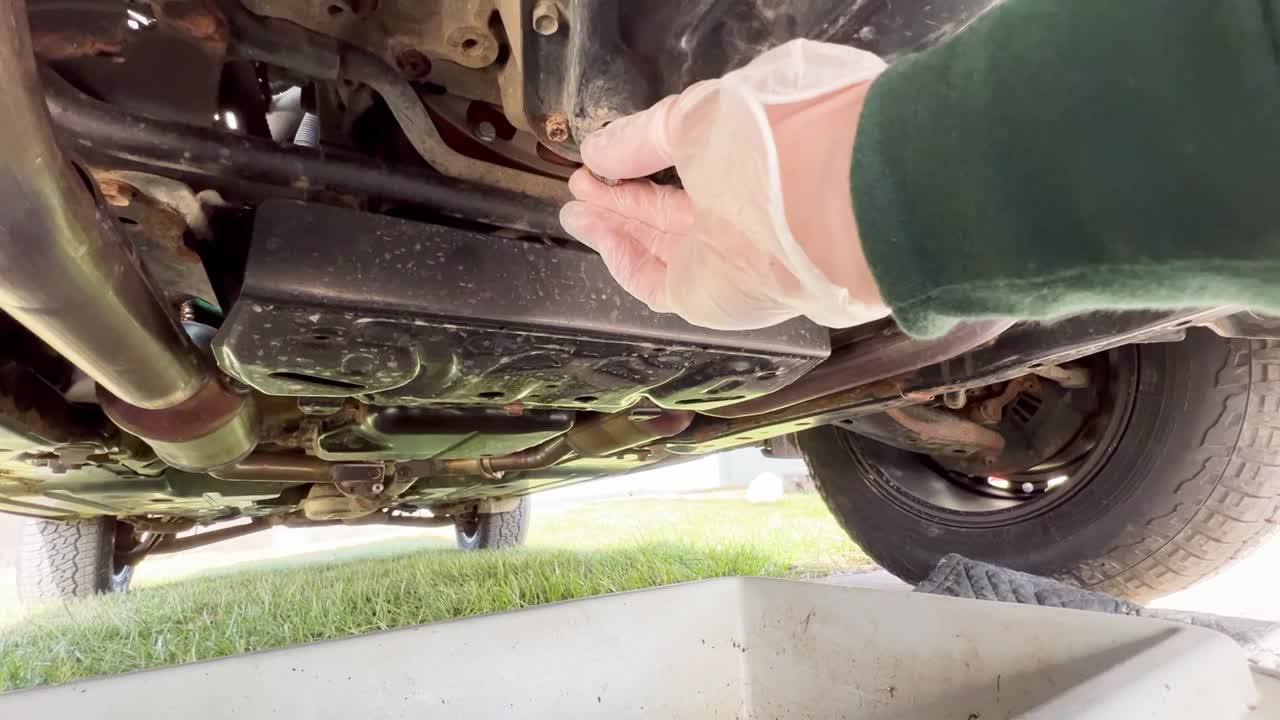 Unplugging an oil pan from the bottom of an SUV wearing a rubber glove