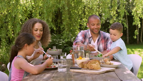 Familia-En-Casa-Comiendo-Comida-Al-Aire-Libre-En-El-Jardín-Juntos