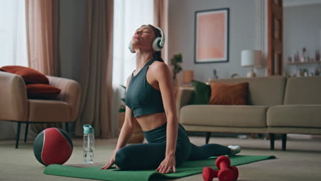 athlete woman workout headphones at sport mat home. slim sportswoman stretching