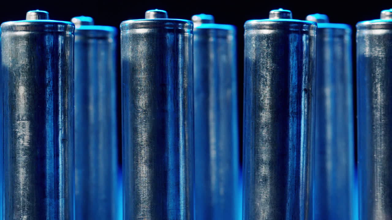 Silver batteries AA and AAA in neon light close-up. Double-A battery is a standard size single cell cylindrical dry battery. Batteries are common in portable electronic devices. An AA battery is composed of a single electrochemical cell that may be either a primary battery or a rechargeable battery.