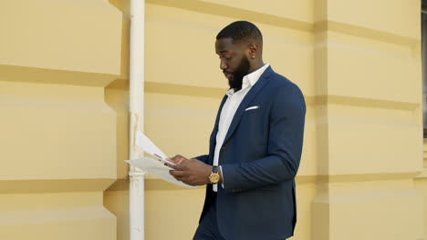 African-businessman-checking-documents-on-city-street.-Afro-man-walking-outside.