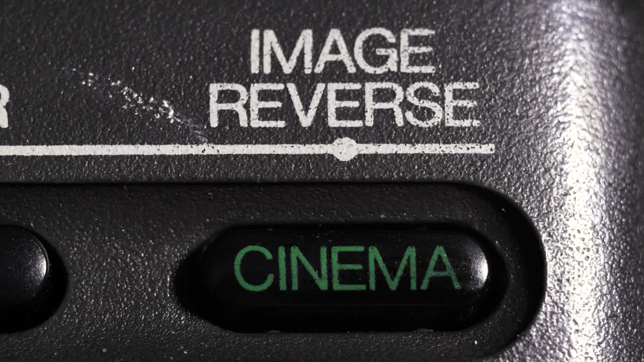 Primo piano del pulsante verde "cinema" e dell'etichetta "inversione immagine" sul pannello nero della videocamera.