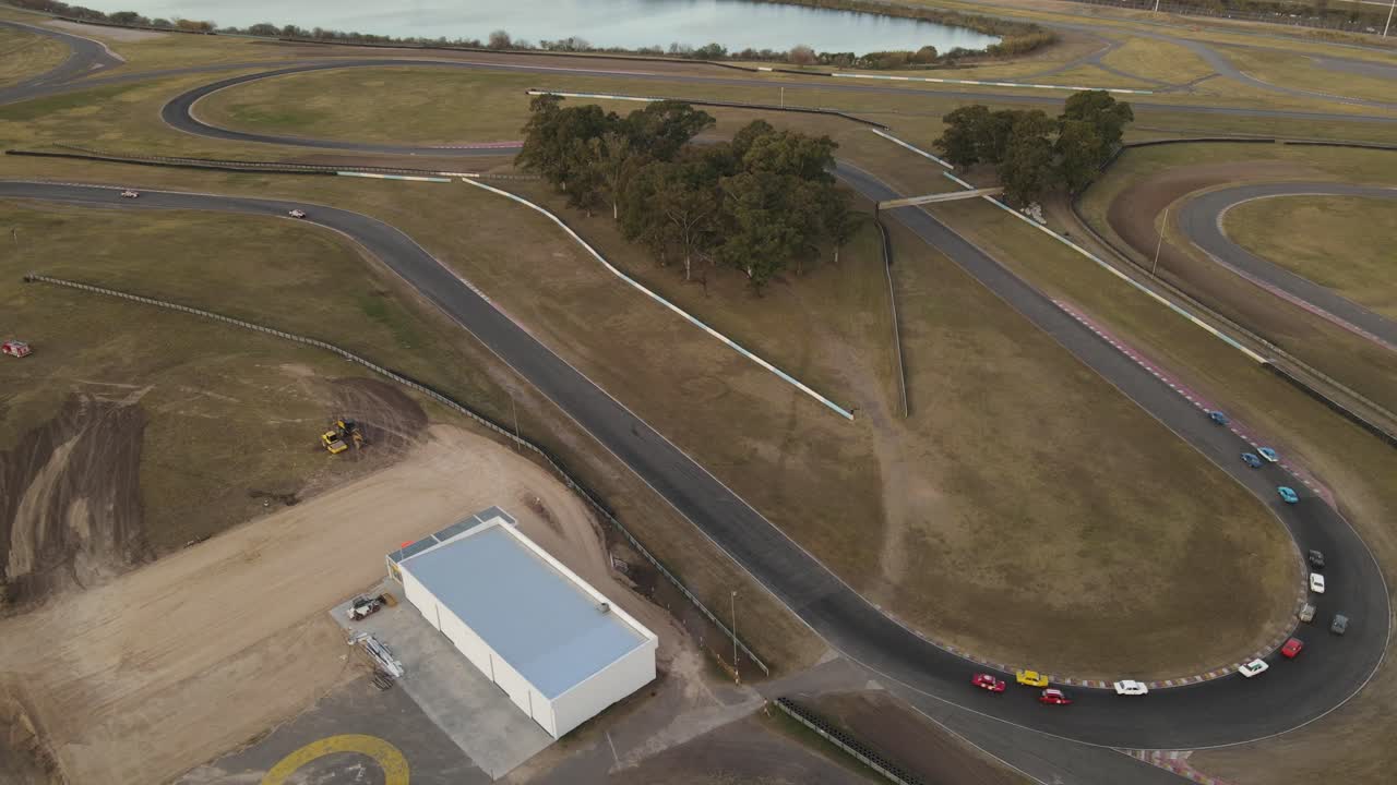 fila de coches de carreras conduciendo con velocidad en la pista de carreras al lado del lago durante el día - autodromo buenos aires - vista aérea