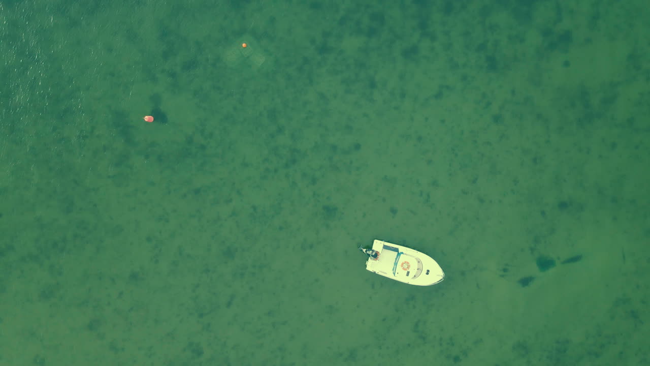 Aerial top down rotate around white boat on green sea water