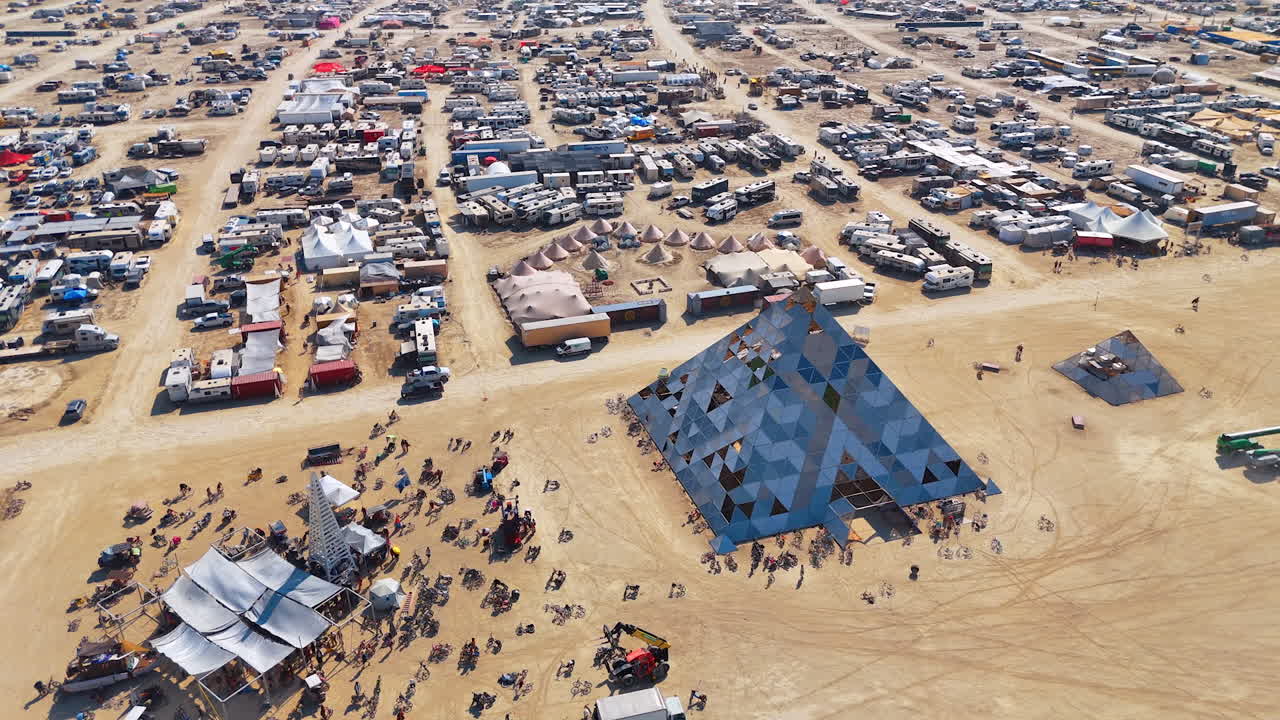 Nevada, USA, 22 August 2025: Burning Man pyramid installation in desert camp. Geometric pyramid art structure surrounded by tents and people at Burning Man desert festival