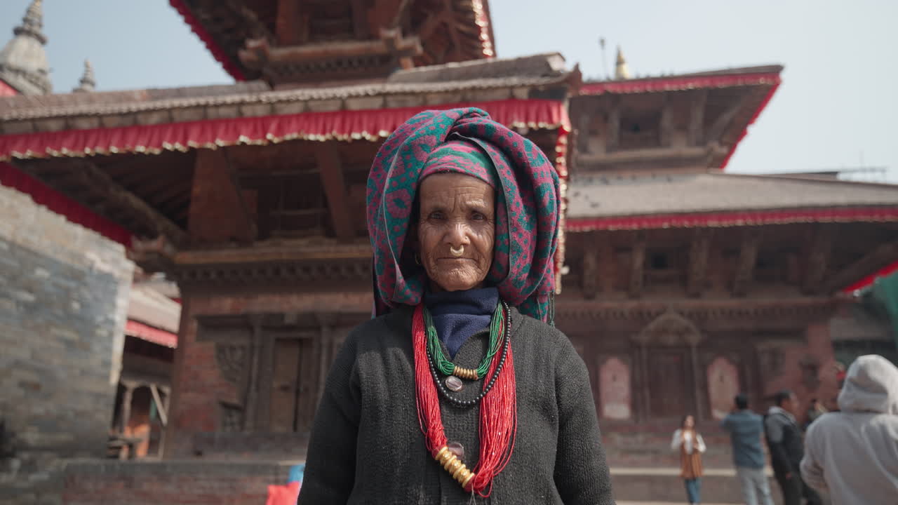 An old Nepali woman wearing a septum nose ring, pote necklace, and traditional outfit stands in front of Kathmandu Durbar Square’s architecture, reflecting Nepal’s cultural heritage and timeless grace