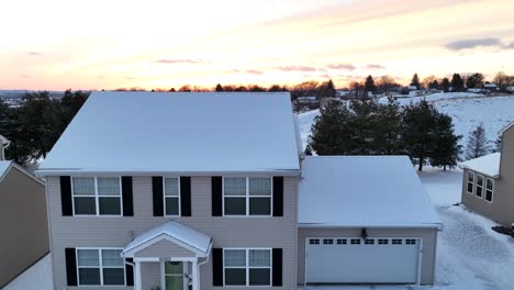 bright orange sunset over a snowy suburban home with a two-car garage