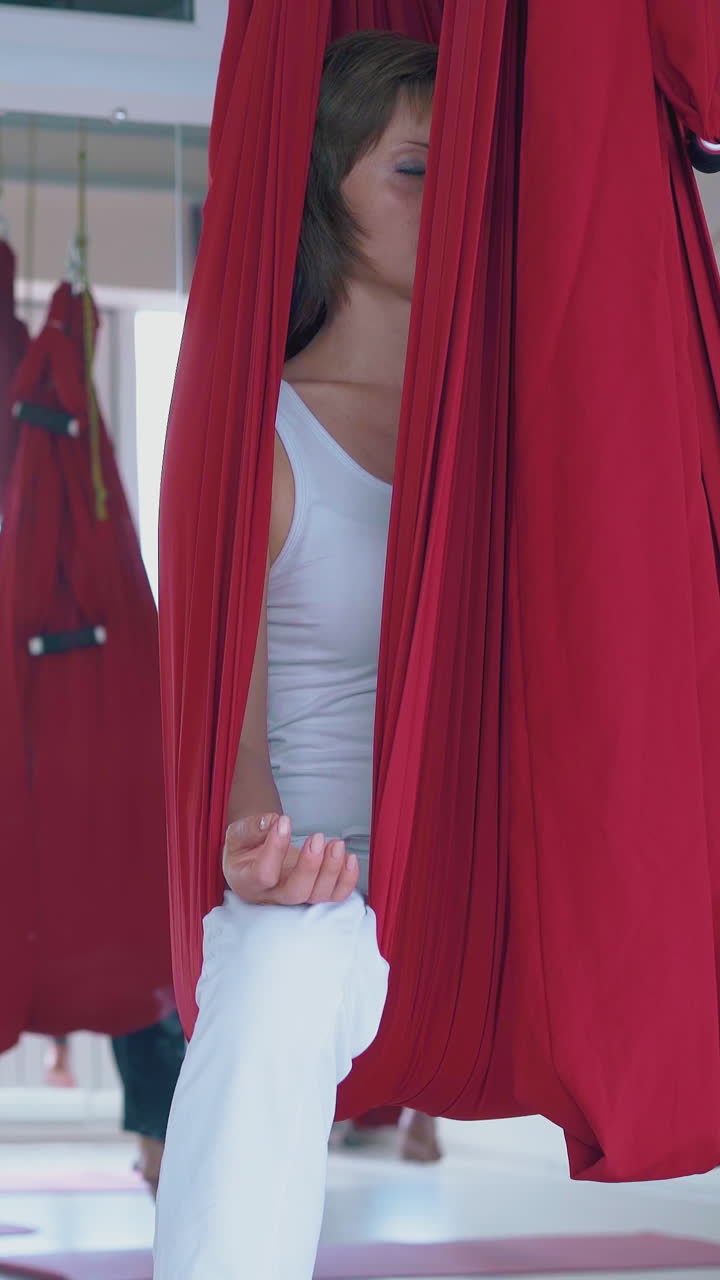 motion along women team practicing breathing exercise holding fingers in mudra position in hammocks close view