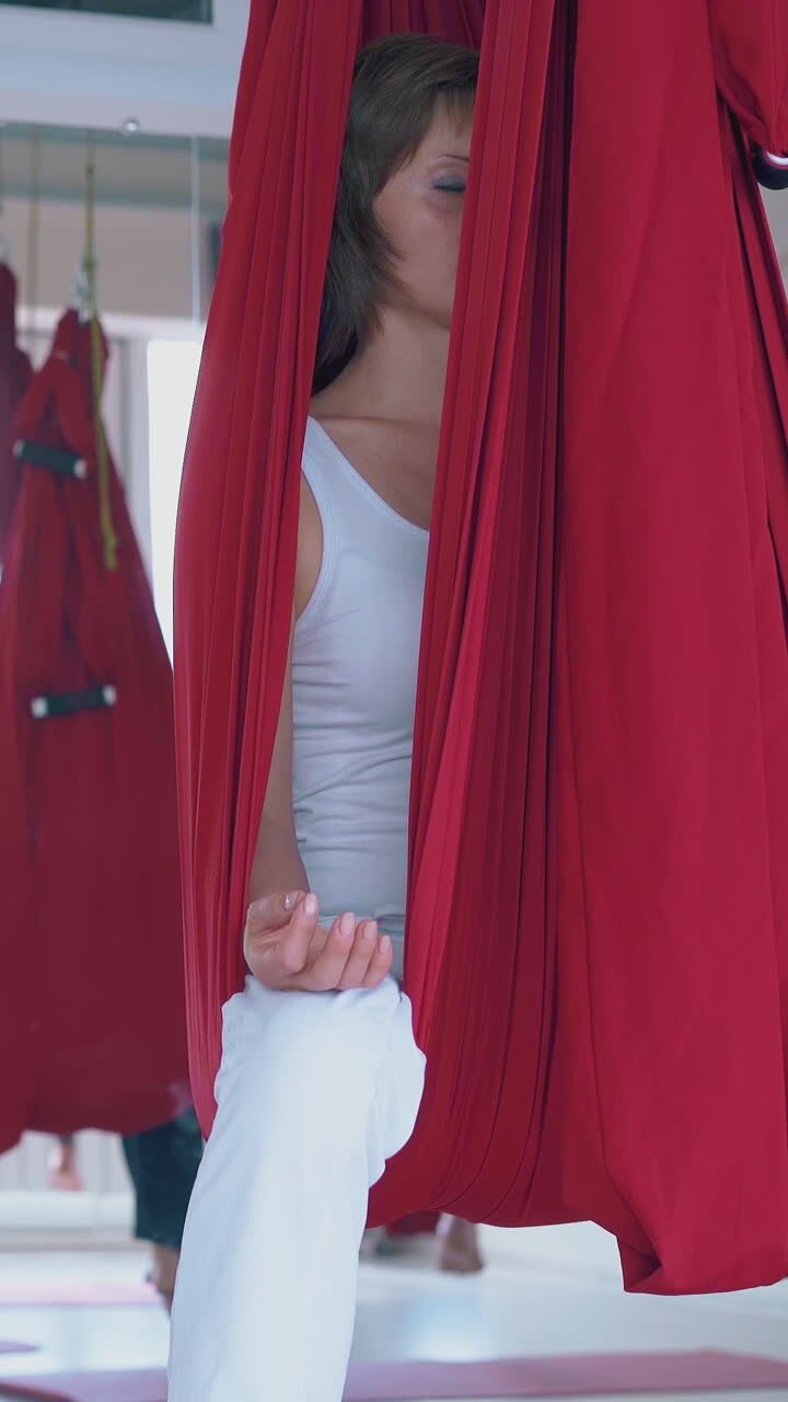 motion along women team practicing breathing exercise holding fingers in mudra position in hammocks close view