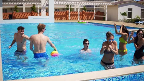 Grupo-De-Jóvenes-Amigos-Jugando-Voleibol-En-La-Piscina.-Fiesta-En-La-Piscina-De-Verano.-Tiro-En-Cámara-Lenta