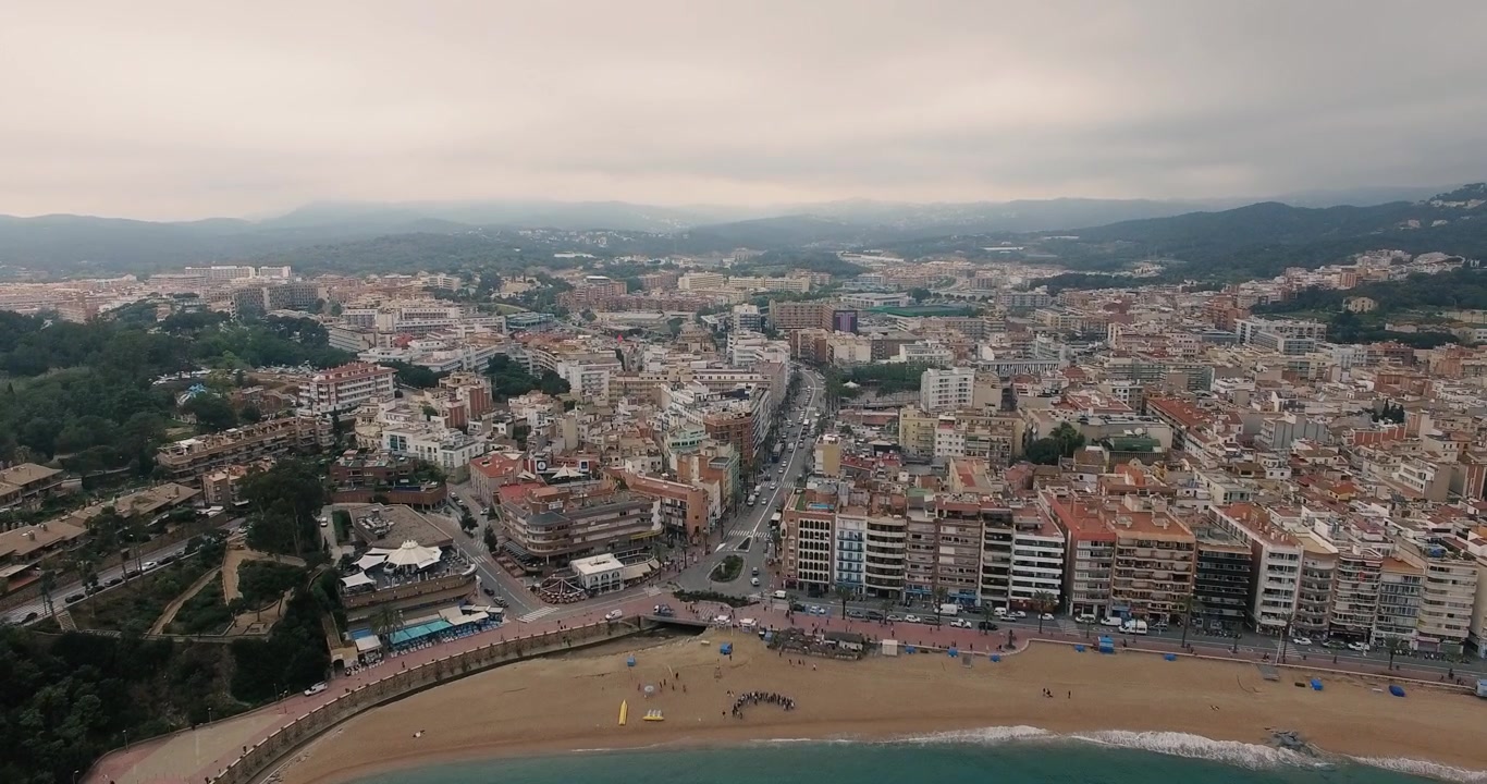 Drone flyver mod vandfronten i Lloret de Mar og afslører stranden, promenaden, bymidten og de omkringliggende bakker på Costa Brava, Spanien.