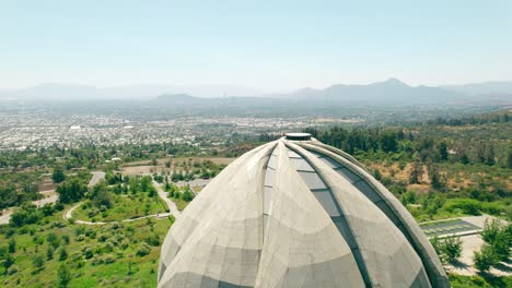 aerial orbit of the top of the bahai temple in south america with the city of santiago in the background, island hills on a sunny day