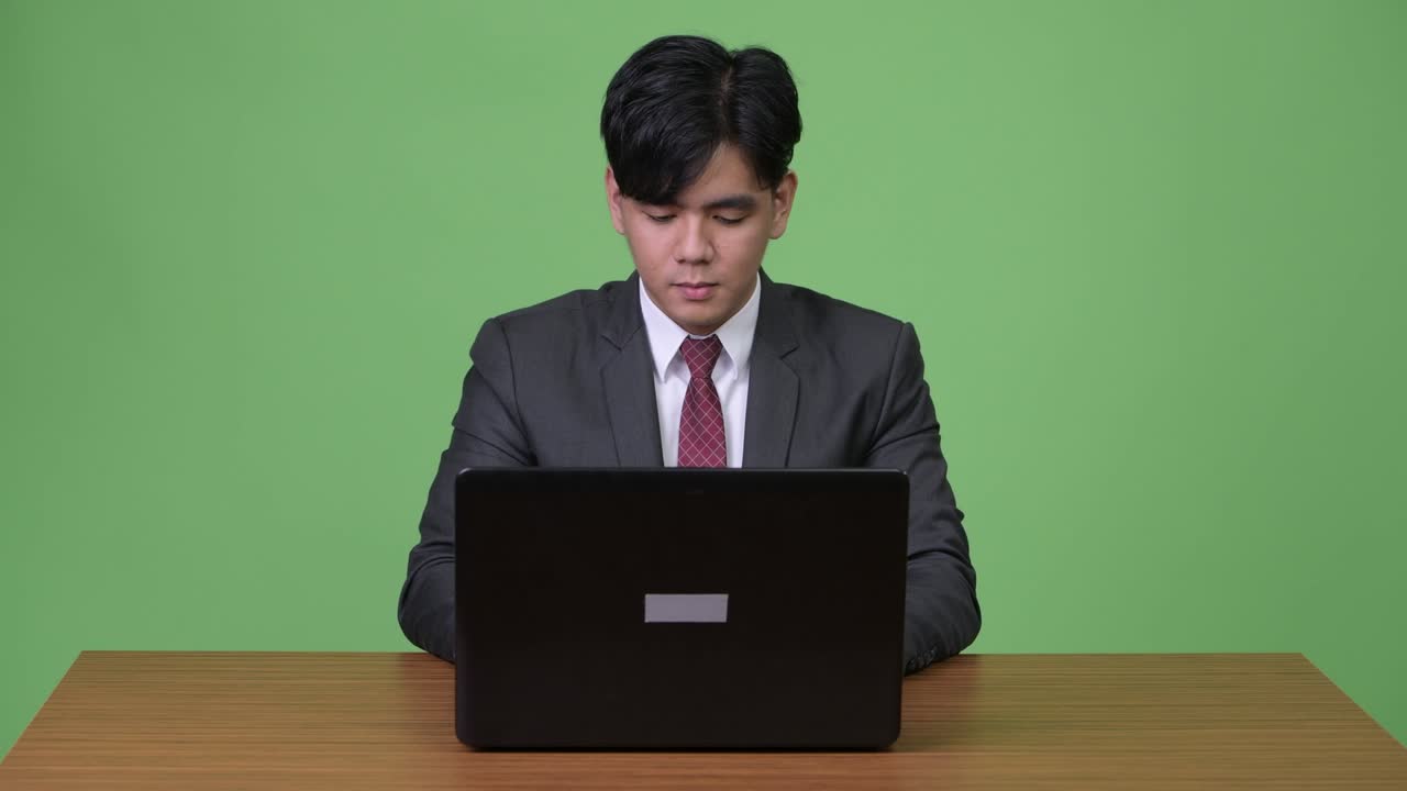 젊은 잘생긴 아시아 사업가가 초록색 배경에 노트북을 가지고 일하고 있습니다.