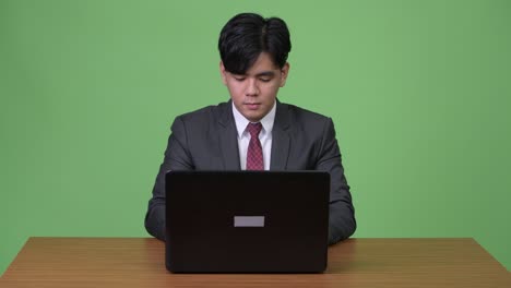 젊은 잘생긴 아시아 사업가가 초록색 배경에 노트북을 가지고 일하고 있습니다.